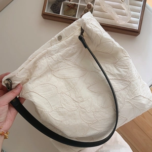 Close-up of beige cotton tote bag featuring leaf embroidery and black leather strap