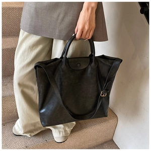 Detailopname van een grote zwarte leren tote bag met drukknoopsluiting in een lifestyle-setting