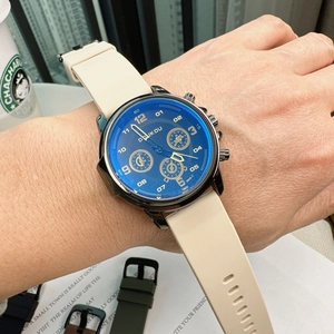 Close-up of a blue dial watch with white silicone strap worn on a wrist in a soft light setting