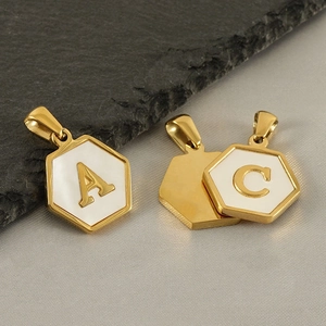 Macro shot of 18k gold hexagon pendants with white shell inlay and embossed letters