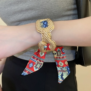 Close-up of golden embossed cuff bracelet with colorful silk scarf ribbon tied in a bow