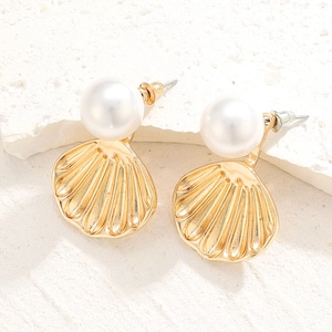 Detailed view of sea shell earrings with white pearls on a textured stone surface