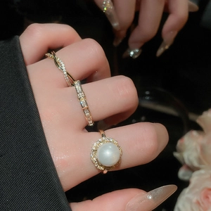 Detailed view of layered gold rings featuring a round pearl and sparkling zircon accents