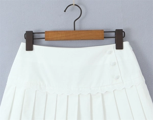 Dettaglio gonna a pieghe bianca con bordo in pizzo, bottoni decorativi e cerniera nascosta
