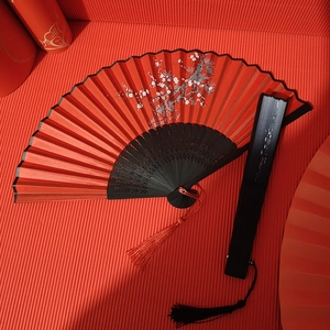 Classic Chinese folding fans with plum blossom patterns and silk tassels on red background