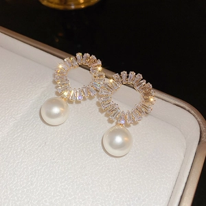Macro shot of gold plated hoop earrings with baguette zircon crystals and pearl drop