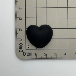 Close-up of black heart resin accessory with size measurement on a grid cutting mat