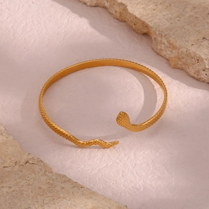 Detailed view of a gold snake-shaped open bangle on a beige stone surface