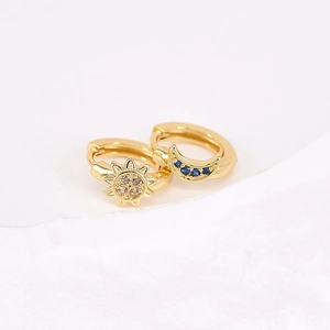 Detail of asymmetric gold huggie earrings featuring sun and blue zircon moon charms