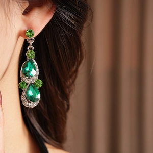 Close-up of vintage teardrop earrings with green faceted gems and shimmering rhinestones