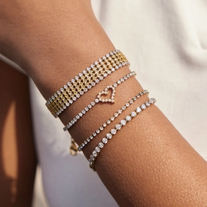 Dettaglio di bracciali tennis sovrapposti in oro e argento con ciondolo a cuore in zircone