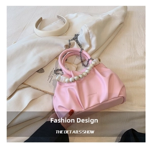 Detail of pink pleated cloud bag featuring pearl handle and metallic chain strap