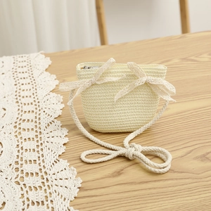 Close-up of a cream woven straw mini bag with delicate white lace bows and rope strap