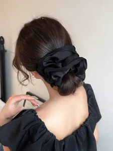 Close-up of a large black satin scrunchie worn in a French-style hair bun on a woman
