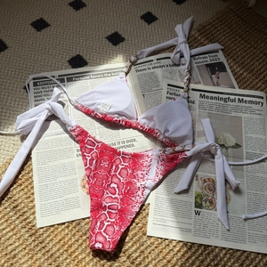 Détail d'un bikini imprimé serpent rouge avec chaînes en métal doré sur fond de journaux