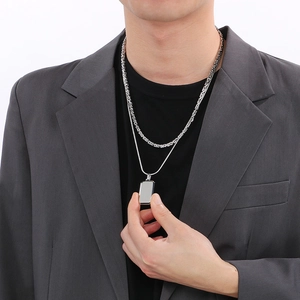 Detail of layered stainless steel necklaces with rectangular tag on charcoal suit jacket