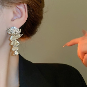 Elegant layered silver fan-shaped shell earrings on a model with metallic texture