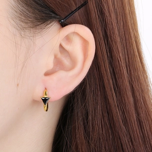 Close-up of minimalist gold earring with a black triangle element worn on the ear