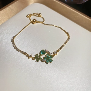 Detail of gold-plated flower bracelet with green heart elements and zircon inlay