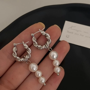 Detail of twisted silver hoop earrings with a gradient of three dangling white pearls