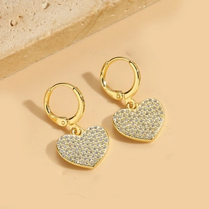 Close-up of gold heart earrings with pavé crystals on a textured stone display