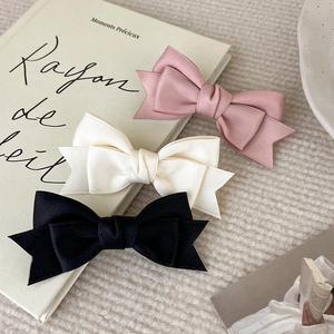 Three satin ribbon bow hair clips in pink, beige, and black on a decorative background