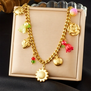 Détail d'un bracelet doré avec pendentifs de fleurs et fruits colorés sur coussin beige