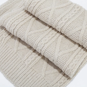 Close-up of beige cable knit scarf texture showing intricate diamond weave patterns