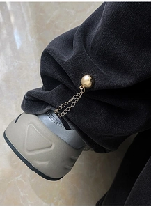 Macro detail of a golden magnetic chain buckle used to shorten black denim trouser cuffs