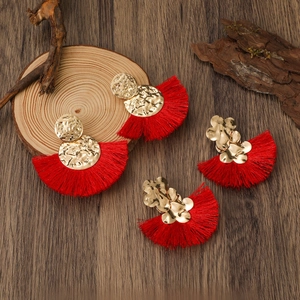 Detalle de pendientes de abanico con borlas rojas y flores de metal martillado oro