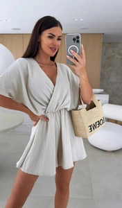 Dettaglio di una tutina con scollo a V, trama plissettata e vita stretta color beige