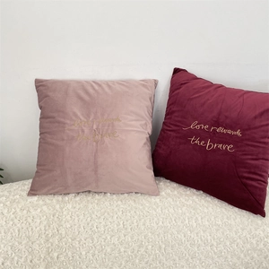 Close-up of velvet pillow covers featuring gold embroidered love rewards the brave text