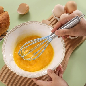 Sky blue silicone whisk with stainless steel handle used in a white ceramic mixing bowl