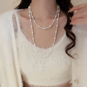 Detail of layered vintage pearl long necklace on a white knit sweater with soft lighting