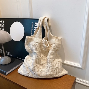 Detail of cream knit tote bag showing thick textured weave on a wooden table