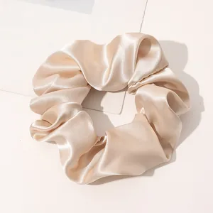 Detail of a champagne gold satin silk scrunchie with shiny texture and soft pleats
