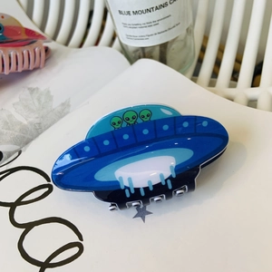 Creative acrylic UFO hair claw clip with green cartoon alien motifs on an open book