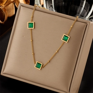 Elegant gold titanium necklace with three square emerald zircons on a beige display pad
