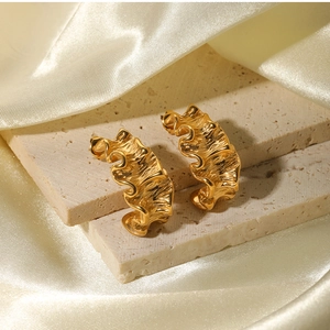 Close-up of gold irregular wavy earrings with textured finish on a stone and silk