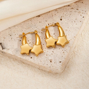 Macro detail of gold star earrings on stone pedestal with cream silk fabric background
