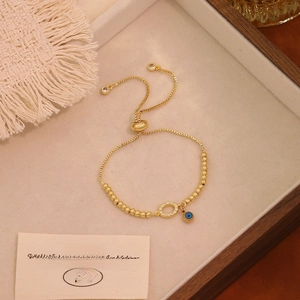 Dettaglio del bracciale a perline dorate con ciondolo malocchio e anello in zircone