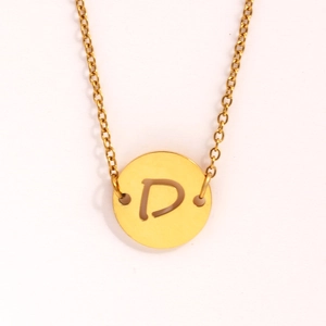 Gros plan d'un collier doré en acier inoxydable avec pendentif rond évidé lettre D
