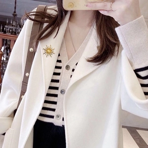 Elegant gold sun-shaped brooch with yellow gemstone on beige coat lapel