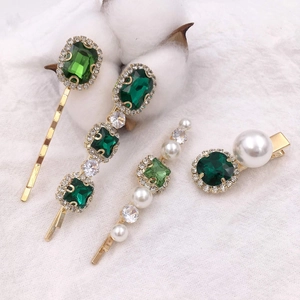 Detail view of vintage gold hairpins with emerald green stones and white pearls on fabric