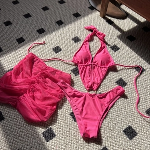 Three-piece hot pink bikini set featuring a halter top, metal ring bottoms, and mesh cover-up