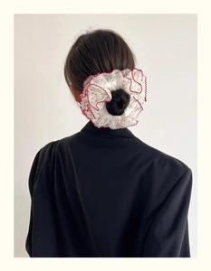 Détail d'un chouchou en mousseline fleurie avec bords rouges porté sur un chignon