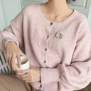 Elegant pink cardigan featuring a round pearl brooch and a delicate gold pendant necklace