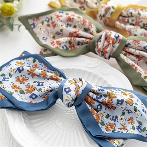 Elegant floral satin bow hair clips in blue and green patterns on a white ceramic plate