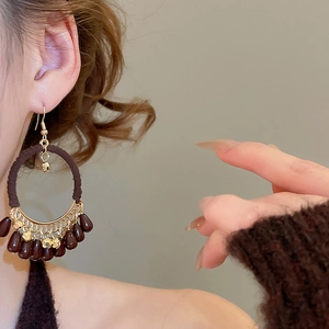 Detail of bohemian cotton-wrapped drop earrings with brown beads worn by a model