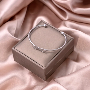 Silver infinity knot open bangle displayed on a premium gift box with satin backdrop